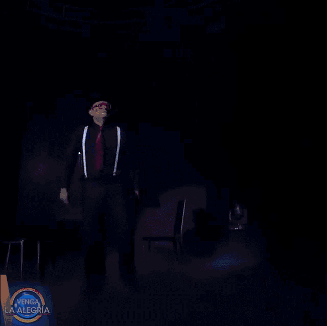 a man in a hat and suspenders is dancing in front of a sign that says " venga la alegria "