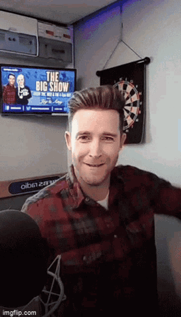 a man in a plaid shirt is smiling in front of a tv screen that says the big show