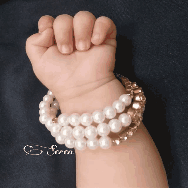 a baby 's hand wearing a pearl bracelet with the name seren written on it
