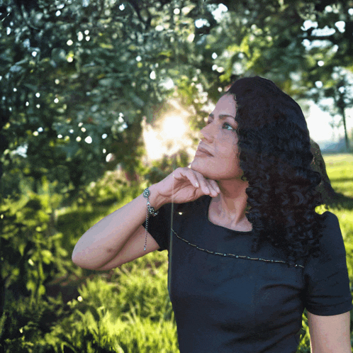 a woman in a black dress is standing in the grass looking up at the sun