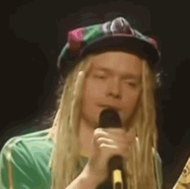 a man with long blonde hair and dreadlocks is singing into a microphone .