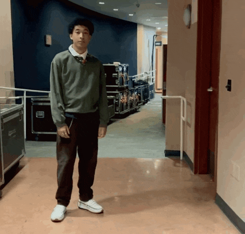 a man in a green sweater stands in a hallway with a sign that says ' a ' on it