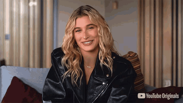 a woman in a black leather jacket is smiling in front of a youtube originals advertisement