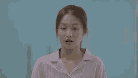 a woman in a pink pajama shirt is making a funny face while standing in front of a blue wall .