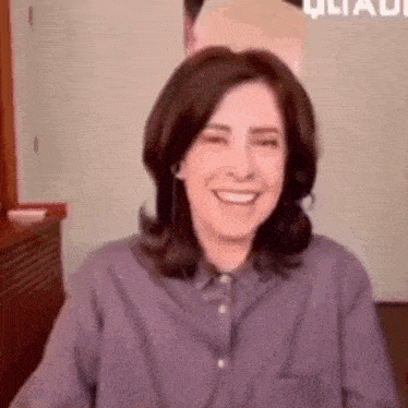 a woman in a purple shirt is smiling while sitting in a room .