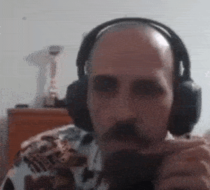a bald man with a beard is wearing headphones while smoking a cigarette .
