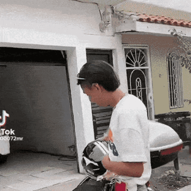 a man is holding a helmet in front of a garage with tiktok written on the bottom right