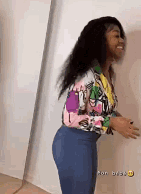 a woman in a colorful shirt and jeans is standing next to a wall .