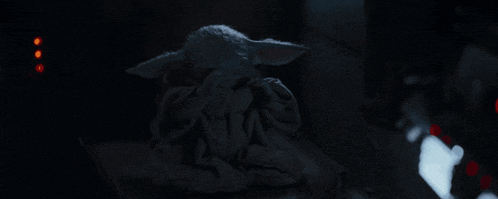 a baby yoda is sitting in a dark room with his eyes closed .