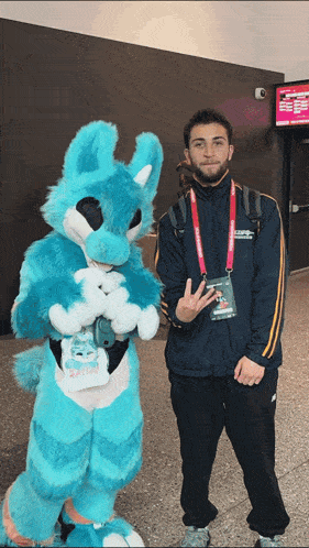 a man standing next to a blue bunny mascot with a lanyard around his neck that says ' sydney ' on it
