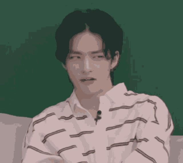 a young man in a striped shirt is sitting on a couch with his eyes closed and a green background .