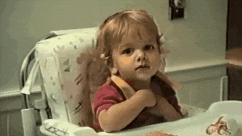 a little girl is sitting in a high chair with her hands folded in front of her chest