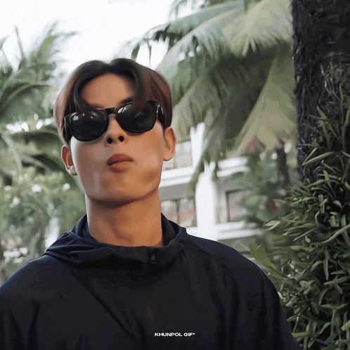 a man wearing sunglasses and a black jacket with khunpol gif on the bottom