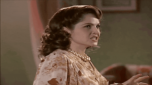 a woman wearing a pearl necklace and a floral dress is making a funny face