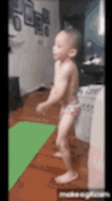 a baby in diapers is dancing on a green yoga mat in a living room .