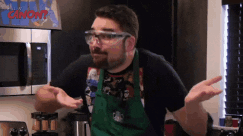 a man wearing a green apron and glasses is standing in front of a microwave that says canon