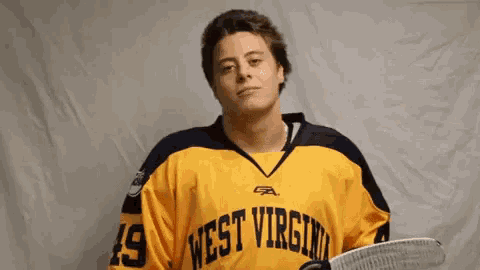 a man wearing a yellow west virginia jersey holds a hockey stick