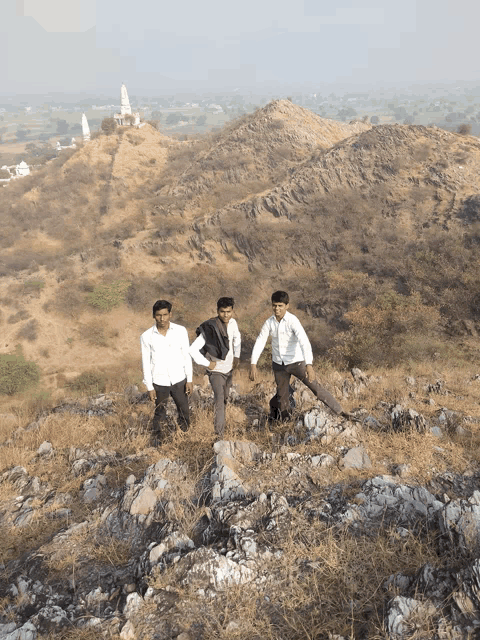three men standing on a rocky hillside with a temple in the background