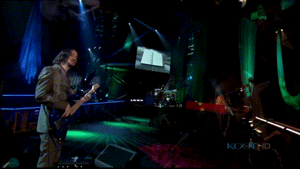 a man playing a guitar on a stage with a screen behind him that says ' kc ' on it