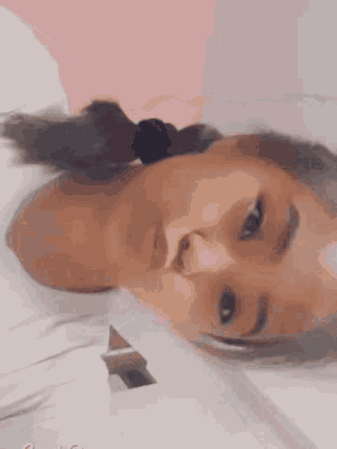 a girl with pigtails is laying on her back and looking at the camera with a pink background .