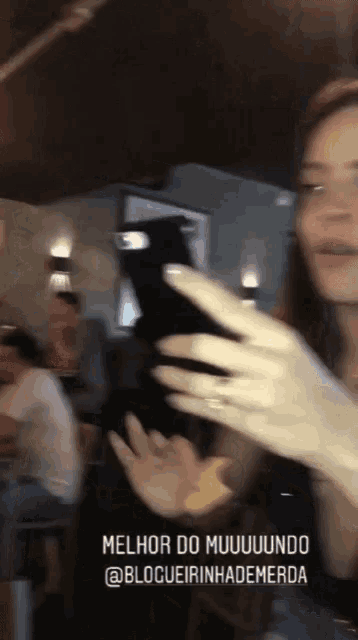 a blurry photo of a woman taking a selfie with the caption melhor do muuuuuuundo @blogueirinhademerda