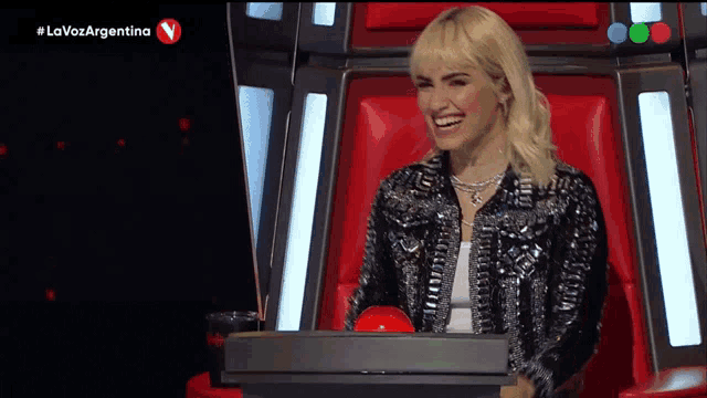 a woman is sitting in a chair with a red button in front of her and the words la voz argentina on the screen behind her