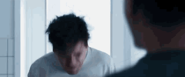 a man in a white shirt is looking at himself in a mirror .