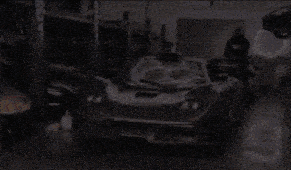 a man in a black hoodie stands next to a black sports car