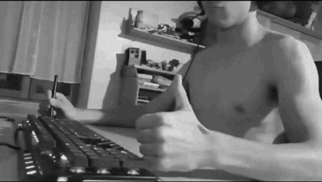 a shirtless man is giving a thumbs up while sitting at a desk with a keyboard