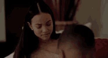 a woman is sitting on a bed next to a man and looking at him .