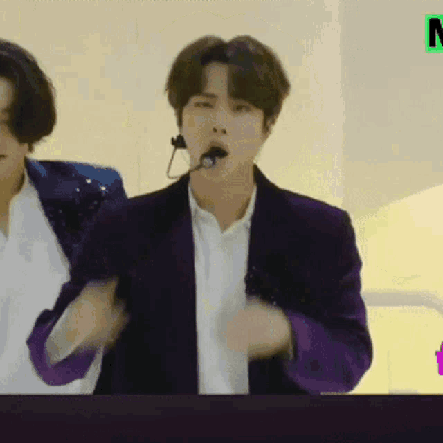 a man in a purple jacket with a microphone in his mouth is standing next to another man in a white shirt .