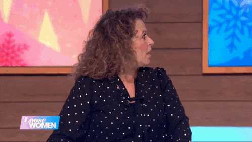 a woman with curly hair is sitting in front of a sign that says " loose women "