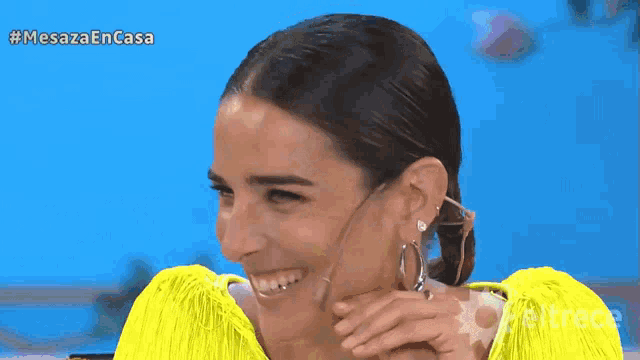 a woman wearing a yellow shirt and hoop earrings is smiling