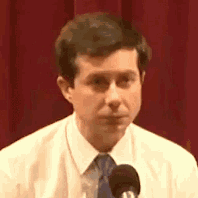a man in a white shirt and tie is speaking into a microphone .