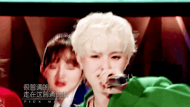 a woman in a green jacket is singing into a microphone with chinese writing on the screen behind her