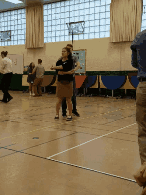 a group of people dancing in a gym with a sign on the wall that says ' basketball '