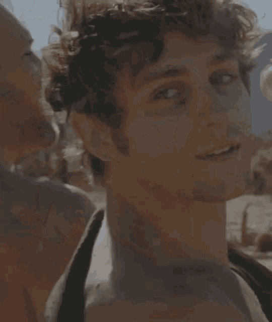a man with curly hair is smiling in front of a tire