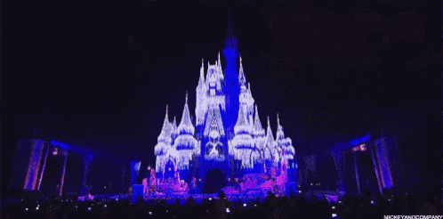 a crowd of people are watching a disney castle being projected on a stage .