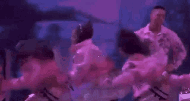 a group of people are dancing on a stage in a pink and purple outfit .