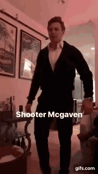 a man in a suit is dancing in a living room with a caption that says shooter mcgaven