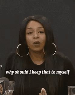 a woman wearing hoop earrings and a black shirt is sitting at a table and talking to herself .