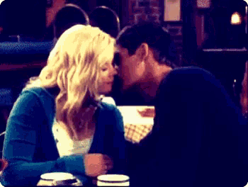 a man and a woman are kissing at a table in a dark room