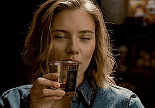 a woman in a denim jacket drinks from a glass