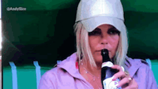 a woman wearing a hat is drinking from a bottle .