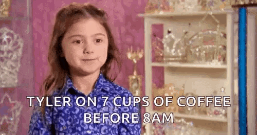a little girl in a blue shirt is sitting in front of a shelf with a shelf of trophies .