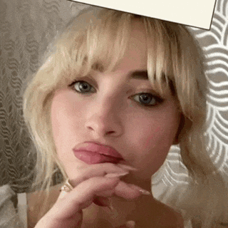 a woman with blonde hair and blue eyes is making a funny face with her hand on her face .