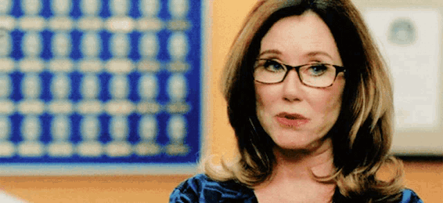 a woman wearing glasses and a blue shirt has a serious look on her face