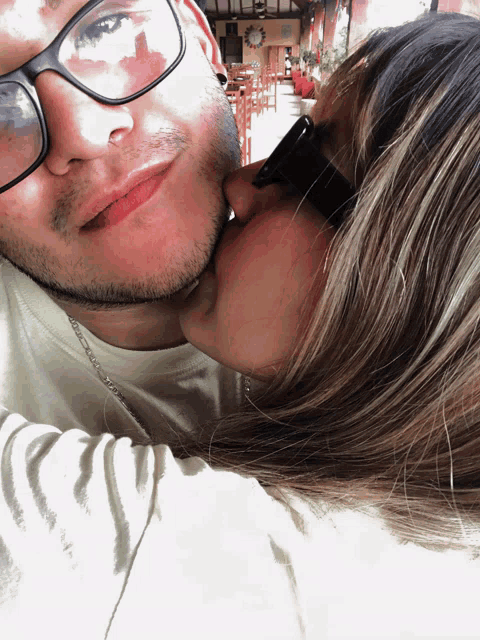 a woman kisses a man on the cheek while he wears glasses