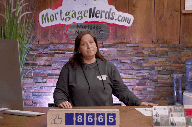 a woman sitting at a desk in front of a mortgage nerds.com sign