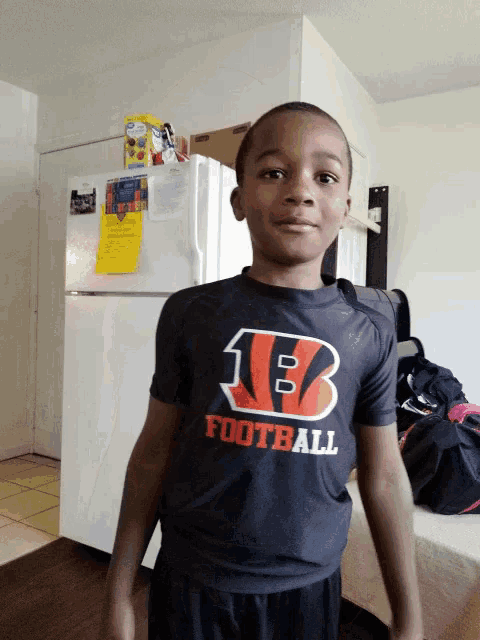 a young boy wearing a black football shirt stands in front of a white refrigerator